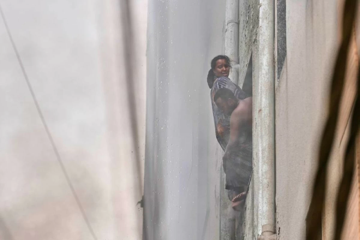 A family of foreign nationals hangs from a hotel window as fire engulfs the building in New Delhi, India, Wednesday, June 3, 2026. (AP Photo/Manish Swarup)