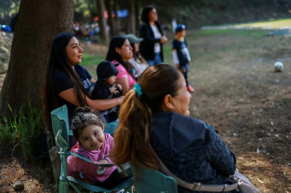 Aitana Michelle Hernandez Blas, 2 years 4 months, and her mother sit as they watch Aitana's father play at the "Cancha de los Dioses" (Field of the Gods), a soccer field inside the crater of the dormant Teoca volcano in the mountains between Xochimilco and Milpa Alta, in Mexico City, Mexico, May 17, 2026. The community flattened the crater more than 60 years ago to build the field, where local amateur teams play matches every Sunday. REUTERS/Raquel Cunha 