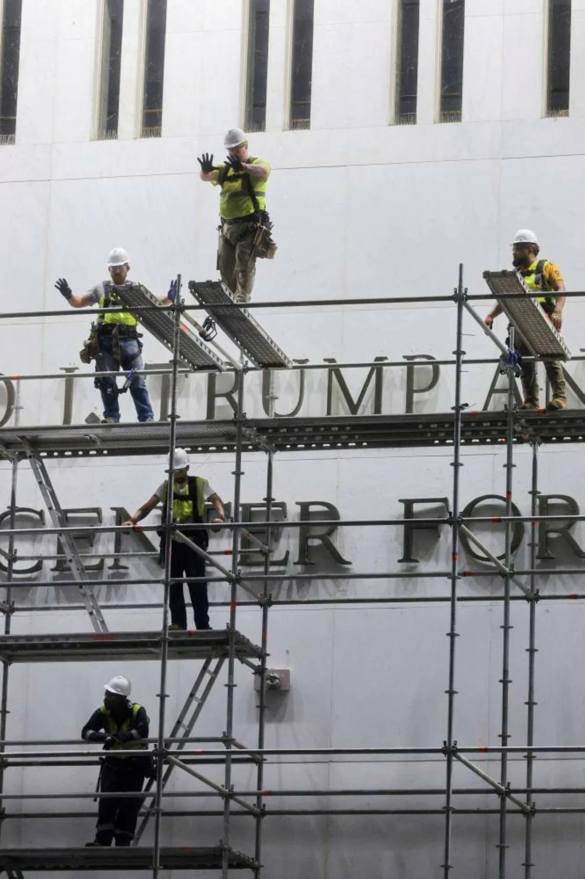 Workers on scaffolding gesture as they prepare ahead of removing lettering from the facade of the John F. Kennedy Memorial Center for the Performing Arts, following a federal judge’s order to remove U.S. President Donald Trump's name from the institution, in Washington, D.C., U.S., June 13, 2026. REUTERS/Jonathan Ernst