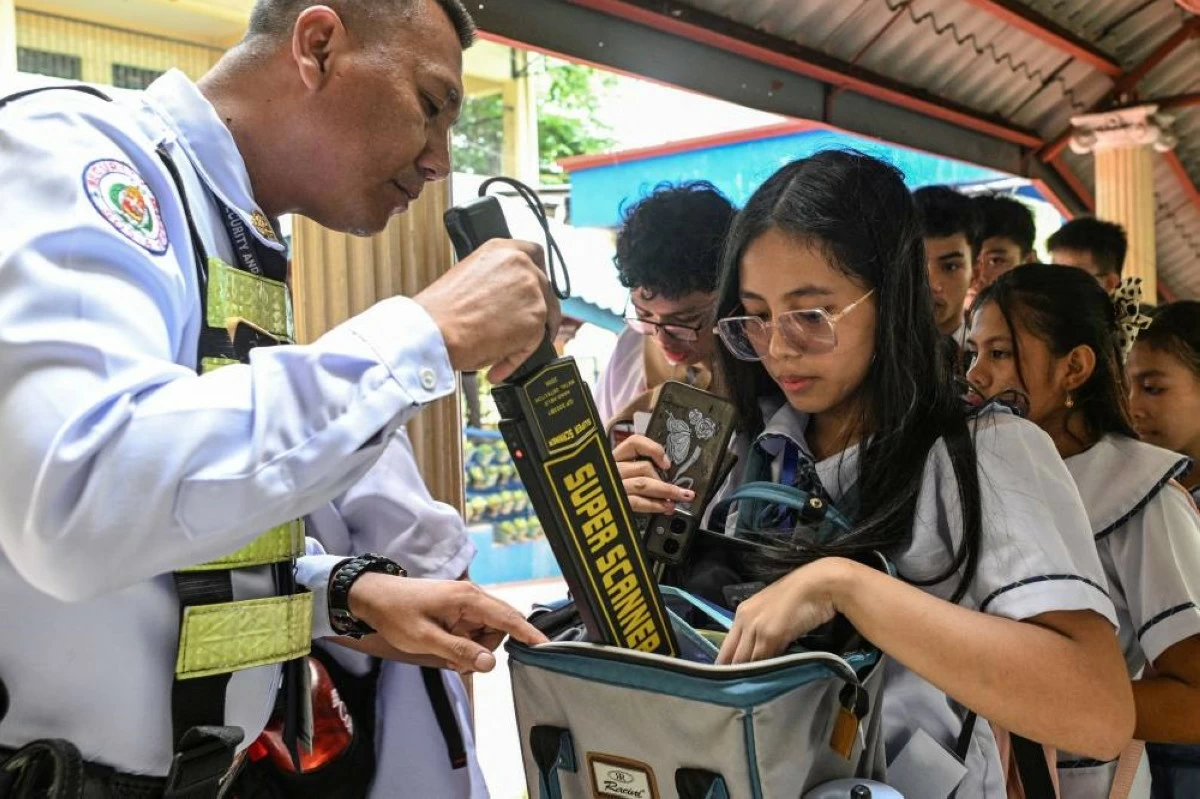 A security guard uses a metal detector as he checks the students' bags as they enter Batasan Hills National High School, a day after at least three students were killed and seven others injured when two students, aged 15 and 14, opened fire at a school in the city of Tacloban southeast of Manila, in Quezon City, Philippines, June 23, 2026. REUTERS