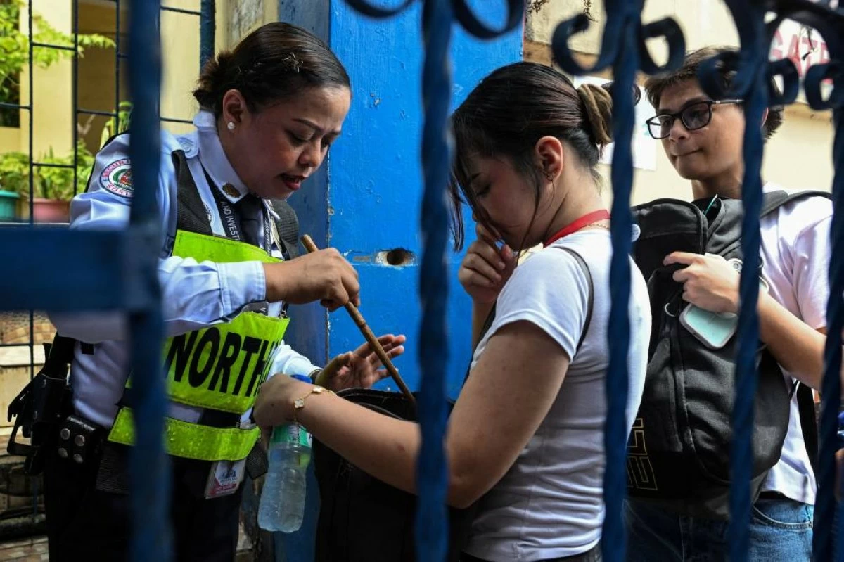 A security guard checks a student's bag as she enters Batasan Hills National High School following deadly shooting that killed 3 students (Reuters)