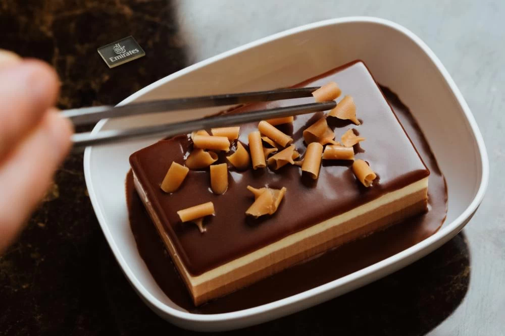 An Emirates Economy Class dessert featuring chocolate - the Emirates' Triple Chocolate Mousse Cake with chocolate sauce and caramel curls.