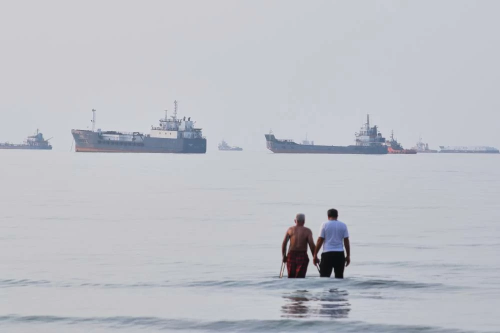 Two men wade in the waters of the Strait of Hormuz with vessels anchored in the background, off Bandar Abbas, Iran, Sunday, July 12, 2026. The United States and Iran on Monday both asserted control over the Strait of Hormuz following a new round of attacks that further escalated tensions in the Gulf region. AP