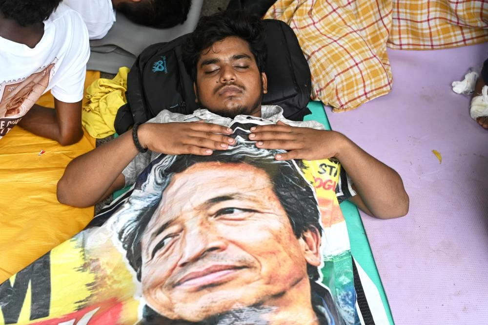 A reclining protestor covers himself with a banner printed with a portrait of Sonam Wangchuk, a prominent activist who was forcefully transferred to a hospital by the police as he staged a hunger strike in support of a movement led by Cockroach Janta Party, at a protest in New Delhi, India, Wednesday, July 22, 2026. (AP)