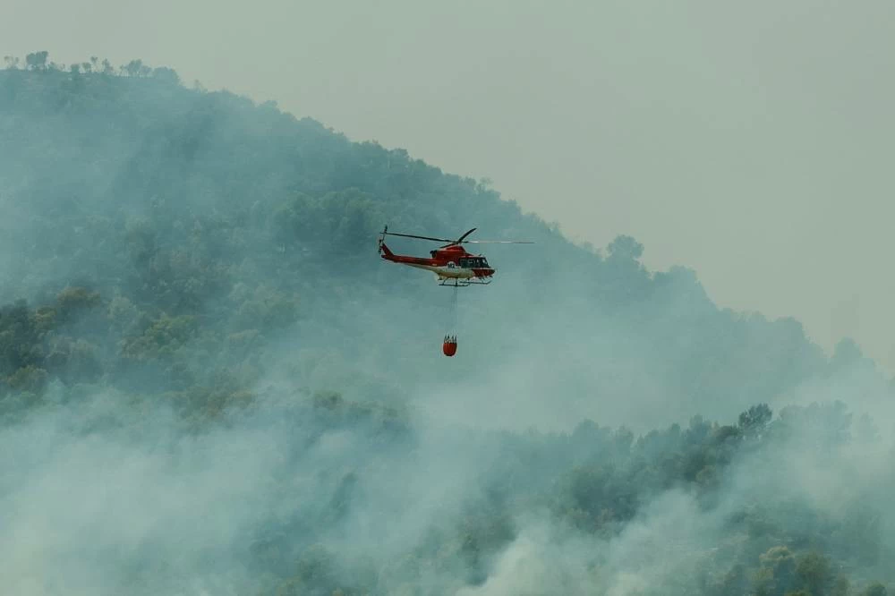 A helicopter flies as smoke rises from a wildfire in Betxi, Spain, July 26, 2026. REUTERS