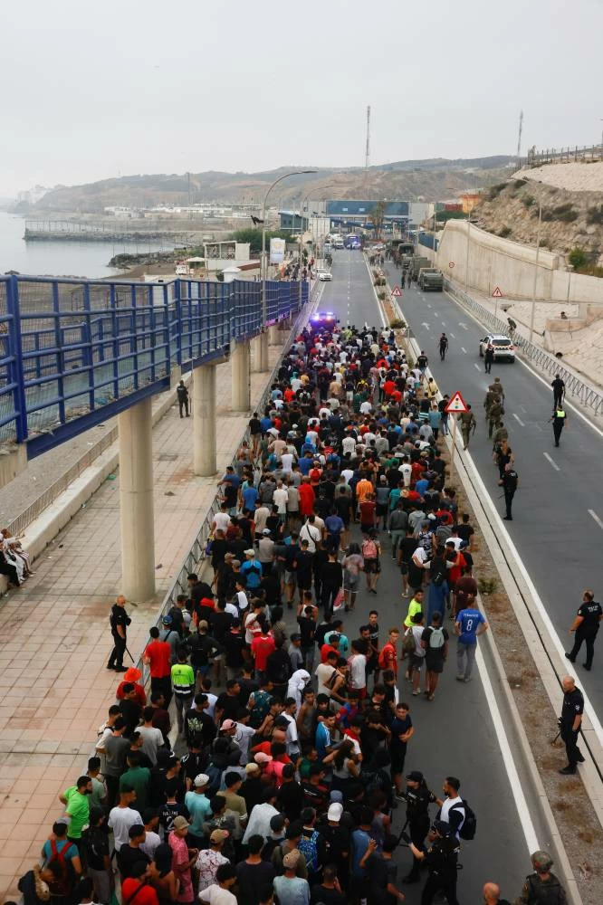 Police officers and Spanish soldiers escort a big group of migrants to the border to take them out of Spain, after mass crossings of migrants on foot and by sea from Morocco into Spanish territory, in Ceuta, Spain, August 1, 2026. (Reuters)