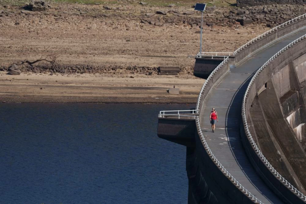 A member of the public crosses a reservoir wall at Baitings reservoir near Sowerby Bridge as water levels drop throughout the country, in Sowerby Bridge, England, Thursday. Picture credit: AP