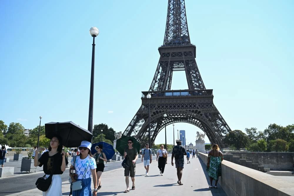Tourists and residents walk along a foot bridge amid a heat wave in Paris, Friday. Picture credit: AP