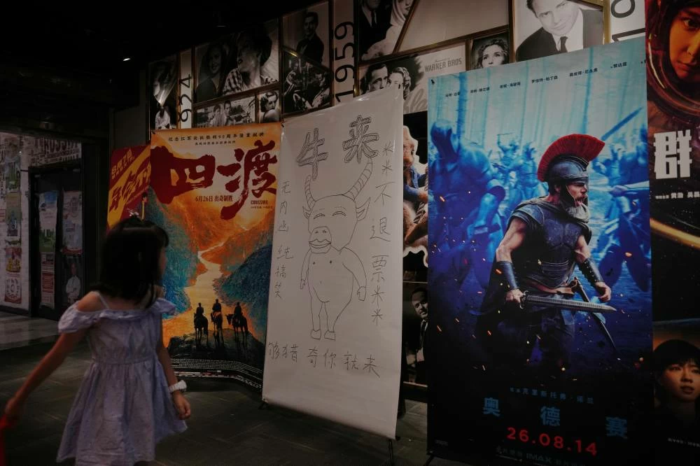 A child looks at a drawing poster promoting a Chinese animated film "Niulai" on display with other movie posters at a cinema in Beijing, Tuesday, Aug. 18, 2026. (AP)