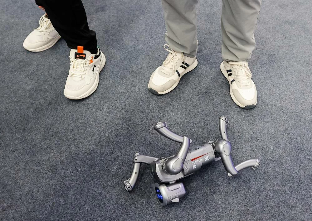 A toy robotic dog lies on the floor next to people's legs at the 2026 World Robot Conference, in Beijing, China, August 19, 2026. (Reuters)