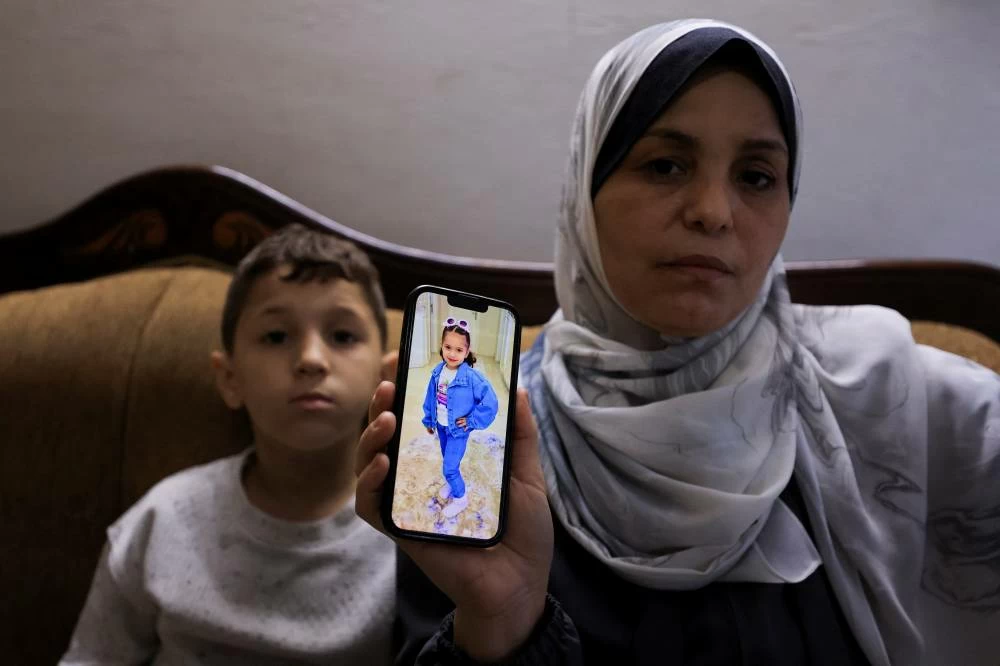 Hind Rajab’s grandmother shows a photo of her on a mobile phone as her grandson Ahmed sits beside her, in Gaza City, August 19, 2026. (Reuters)