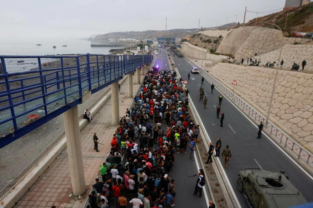 Police officers and Spanish soldiers escort a big group of migrants to the border to take them out of Spain, after mass crossings of migrants on foot and by sea from Morocco into Spanish territory, in Ceuta, Spain, August 1, 2026. (Reuters)