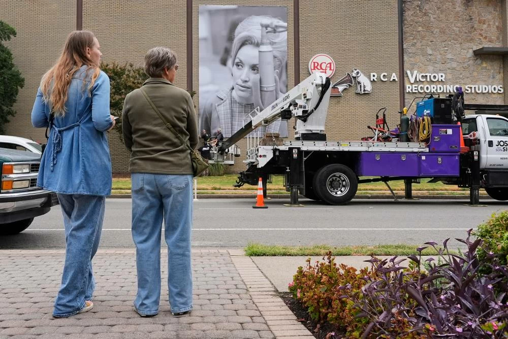 Tourists from Wisconsin, Megan Meyer, left, and Lauren Halmsted, watch a portrait of the late Dolly Parton get installed outside RCA Studio A, Wednesday, Sept. 23, 2026, in Nashville, Tenn. where Parton recorded "Jolene" and "I Will Always Love You" during a 1973 recording session. (AP)