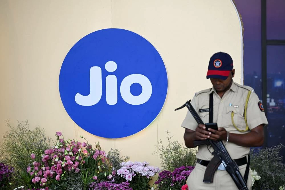 A security officer uses his mobile phone with the Jio logo in the background, during a Jio Platforms Ltd. IPO press conference in Mumbai, India, October 15, 2026. (Reuters)