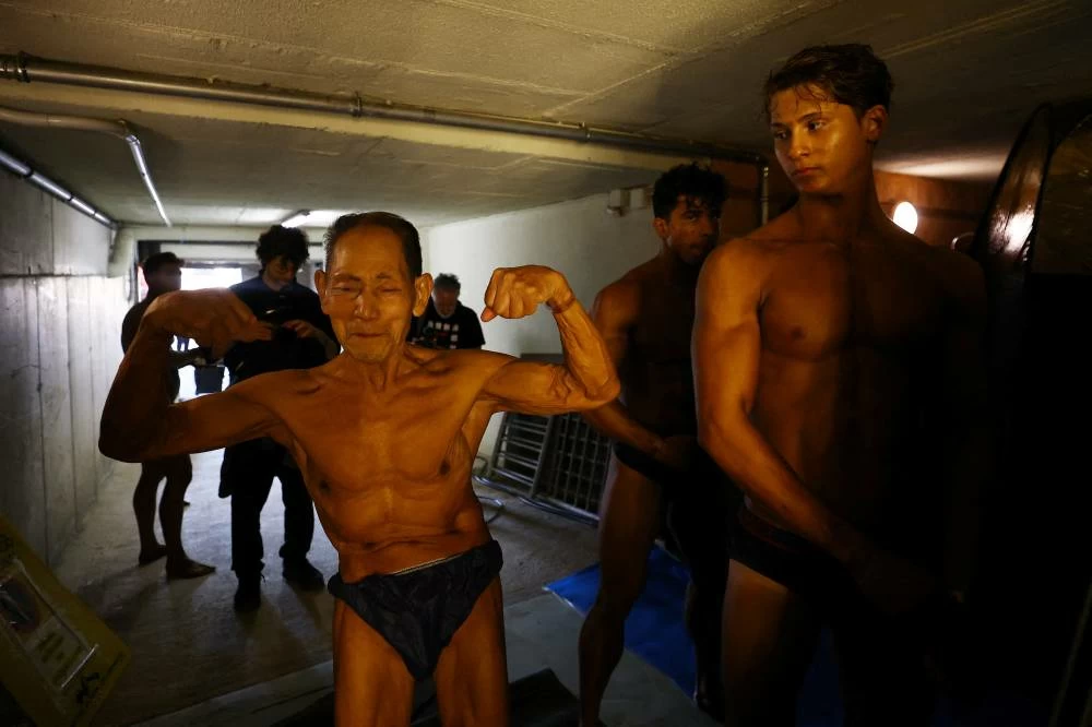 Japan's Toshisuke Kanazawa, 90, waits to receive a spray tan ahead of the IFBB World Fitness Championships in Santa Susanna, Spain, on October 30, 2026, as fellow competitors look on. (Reuters)